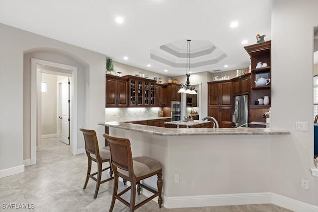 kitchen with pendant lighting, decorative backsplash, kitchen peninsula, and stainless steel refrigerator