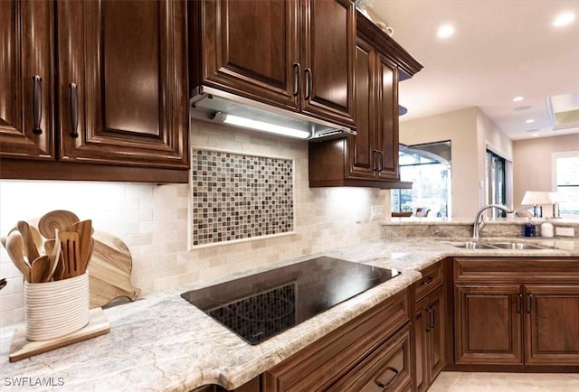 kitchen featuring black electric stovetop, decorative backsplash, light stone counters, and sink