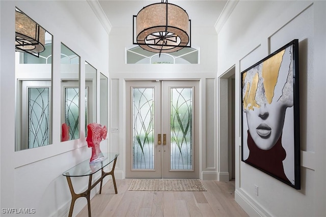 foyer with french doors, light wood-type flooring, ornamental molding, and a high ceiling