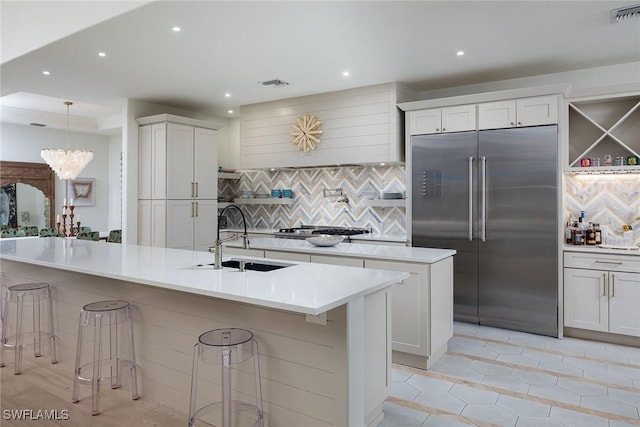 kitchen with sink, stainless steel appliances, a kitchen island with sink, a breakfast bar, and white cabinets