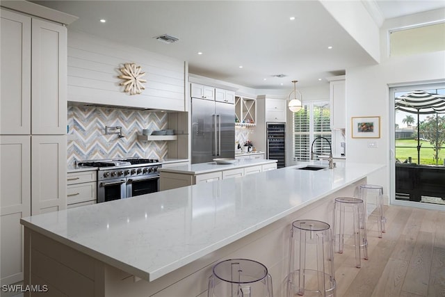 kitchen featuring light wood-type flooring, premium appliances, sink, a large island with sink, and white cabinetry