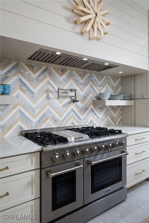 kitchen featuring decorative backsplash, white cabinets, light tile patterned flooring, and range with two ovens