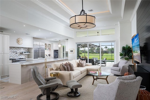 living room featuring a towering ceiling, ornamental molding, a tray ceiling, and light hardwood / wood-style floors