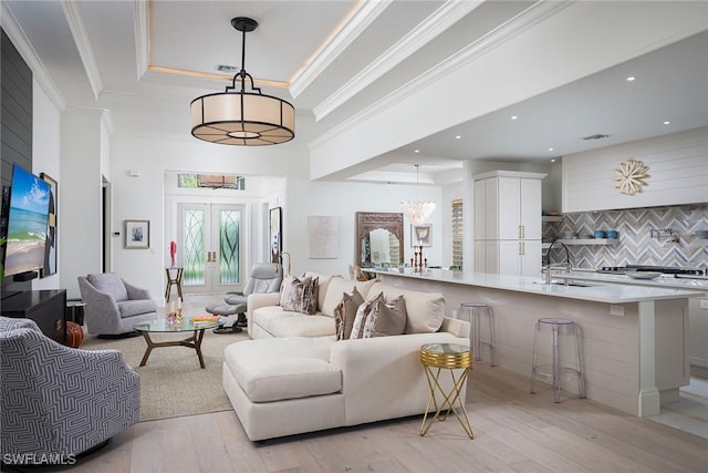 living room featuring sink, light hardwood / wood-style floors, a tray ceiling, crown molding, and french doors