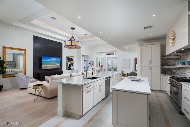 kitchen with sink, appliances with stainless steel finishes, white cabinetry, hanging light fixtures, and an island with sink