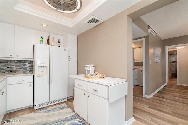 kitchen featuring separate washer and dryer, white cabinets, decorative backsplash, white refrigerator with ice dispenser, and a raised ceiling