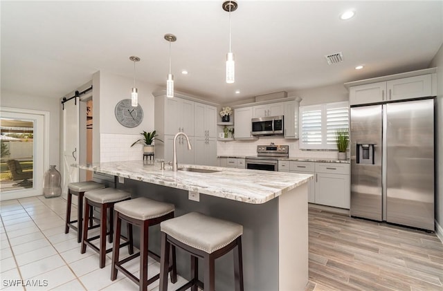 kitchen with a barn door, tasteful backsplash, decorative light fixtures, white cabinetry, and stainless steel appliances