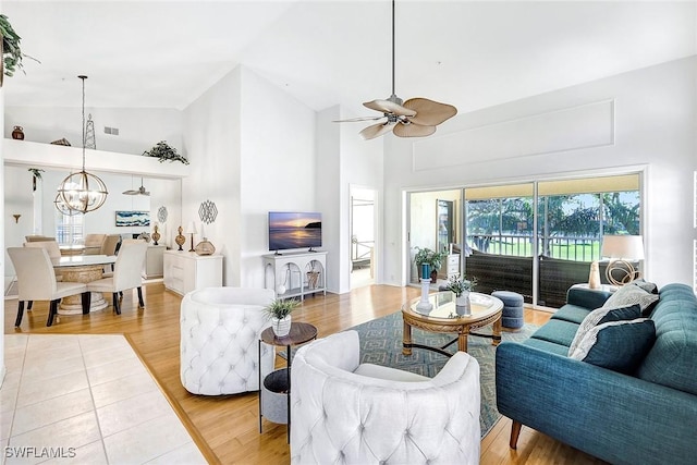 living room featuring ceiling fan with notable chandelier, high vaulted ceiling, and light hardwood / wood-style flooring