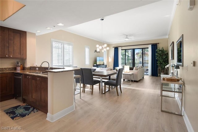 kitchen featuring a breakfast bar, ceiling fan with notable chandelier, sink, light hardwood / wood-style flooring, and kitchen peninsula