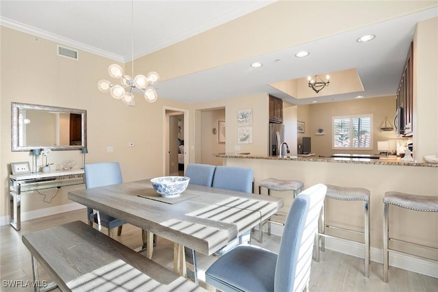 dining room featuring a notable chandelier, a raised ceiling, light wood-type flooring, and crown molding