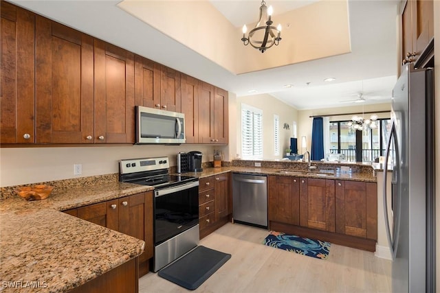 kitchen featuring stone counters, sink, hanging light fixtures, light hardwood / wood-style floors, and appliances with stainless steel finishes