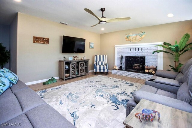 living room featuring ceiling fan, wood-type flooring, and a brick fireplace