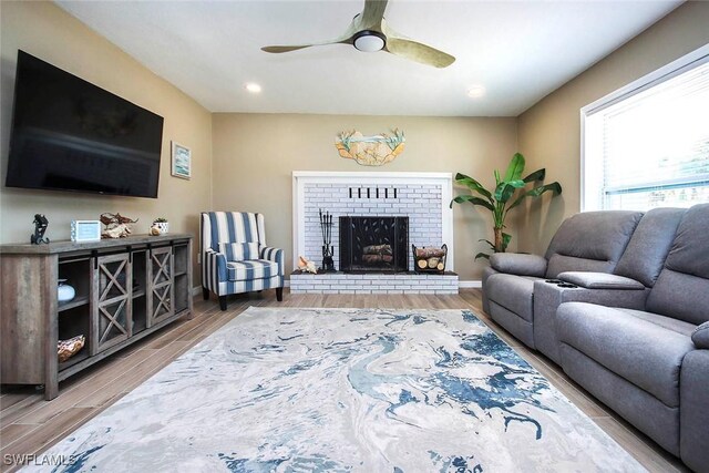 living room featuring ceiling fan, wood-type flooring, and a brick fireplace