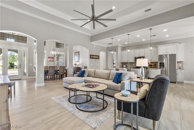 living room with light wood-type flooring, a high ceiling, ceiling fan with notable chandelier, and crown molding