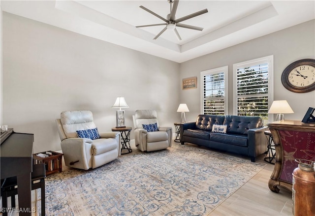 living room with ceiling fan, light hardwood / wood-style floors, and a raised ceiling