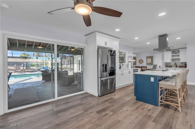 kitchen with white cabinetry, stainless steel fridge with ice dispenser, light hardwood / wood-style flooring, a breakfast bar area, and island range hood