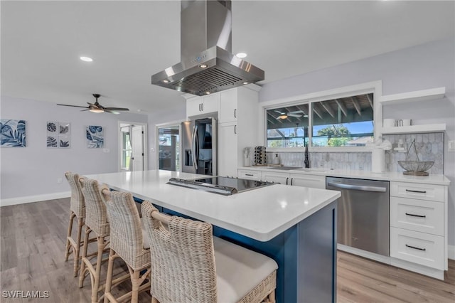 kitchen featuring island exhaust hood, stainless steel appliances, sink, white cabinets, and a kitchen island