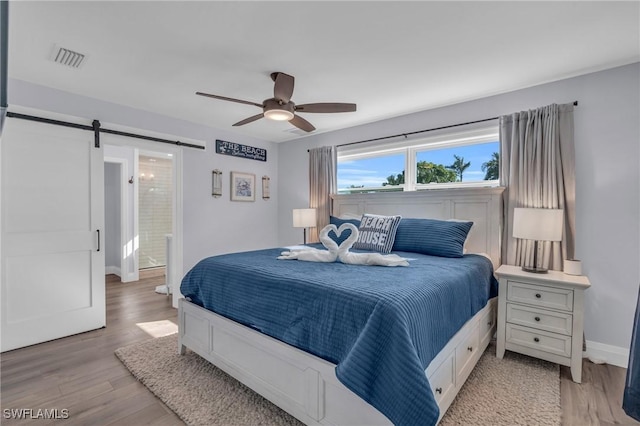 bedroom with ceiling fan, a barn door, light hardwood / wood-style floors, and connected bathroom