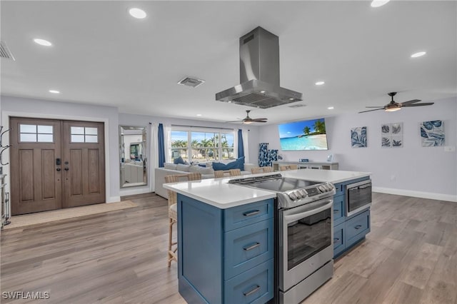 kitchen with a breakfast bar area, light wood-type flooring, blue cabinetry, island range hood, and stainless steel appliances