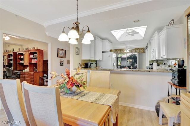 dining space with a skylight, an inviting chandelier, light hardwood / wood-style floors, and crown molding