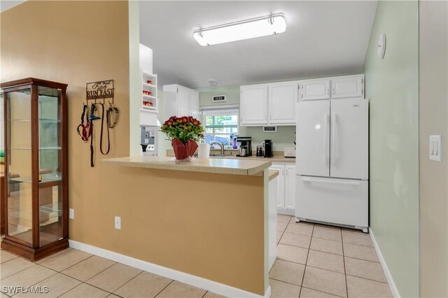 kitchen featuring kitchen peninsula, sink, light tile patterned floors, white refrigerator, and white cabinetry