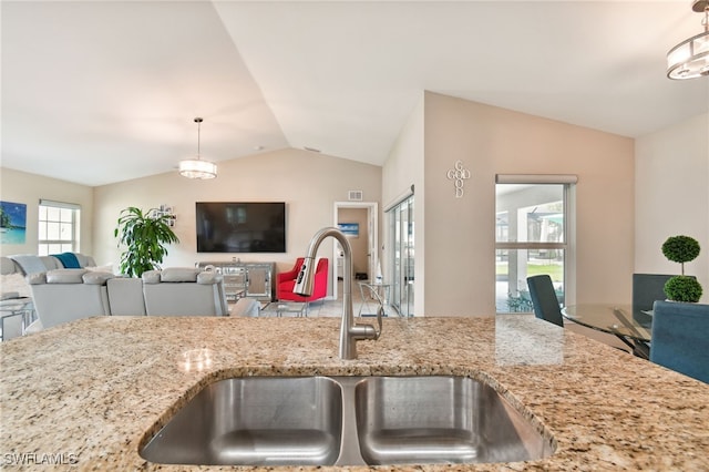 kitchen with pendant lighting, light stone counters, lofted ceiling, and sink