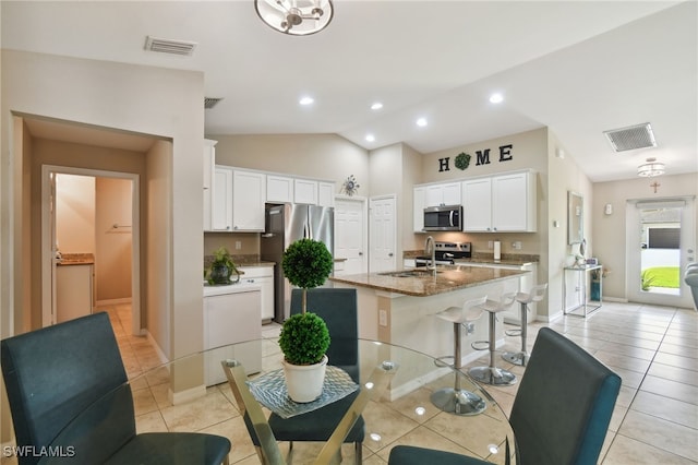 kitchen with stainless steel appliances, vaulted ceiling, stone counters, white cabinets, and an island with sink