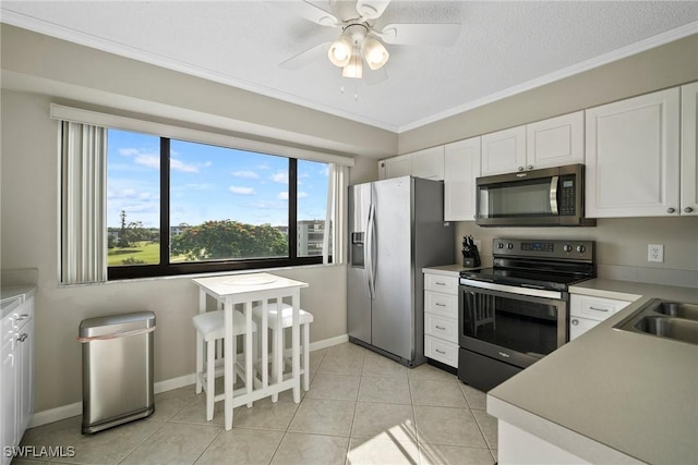 kitchen with appliances with stainless steel finishes, ornamental molding, ceiling fan, light tile patterned floors, and white cabinets