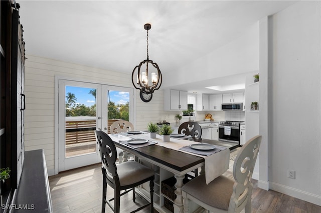 dining room featuring french doors, an inviting chandelier, wood walls, lofted ceiling, and hardwood / wood-style flooring