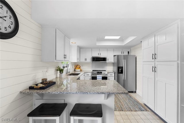 kitchen with kitchen peninsula, a kitchen breakfast bar, stainless steel appliances, and white cabinetry