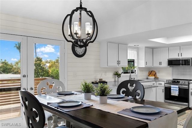 dining area featuring french doors, sink, a chandelier, lofted ceiling, and wooden walls