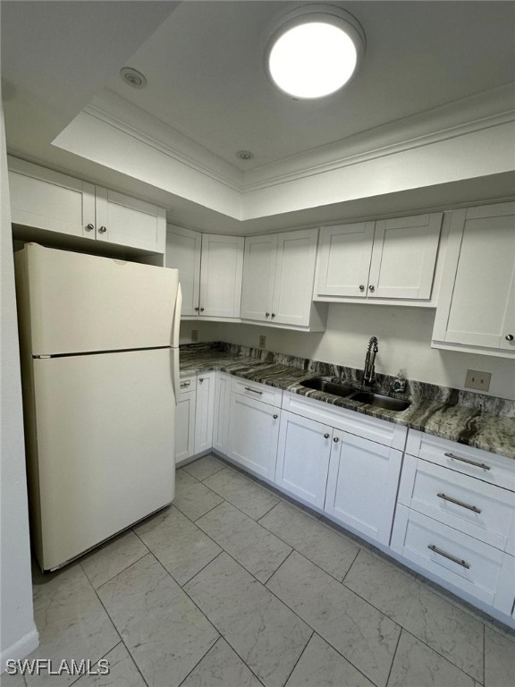 kitchen featuring white fridge, white cabinetry, dark stone counters, and sink