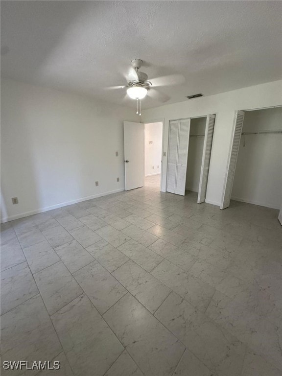 unfurnished bedroom with a textured ceiling, two closets, and ceiling fan