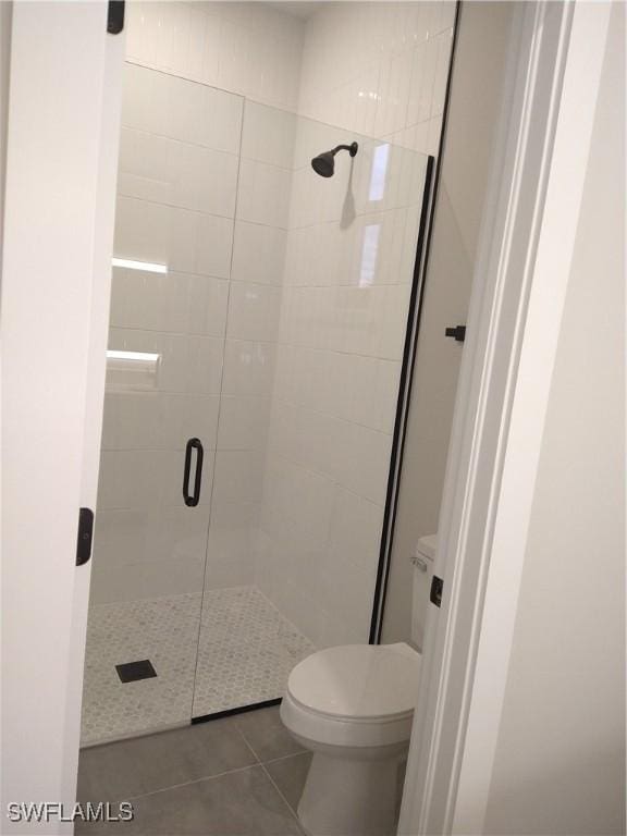 bathroom featuring tile patterned floors, toilet, and a shower with door