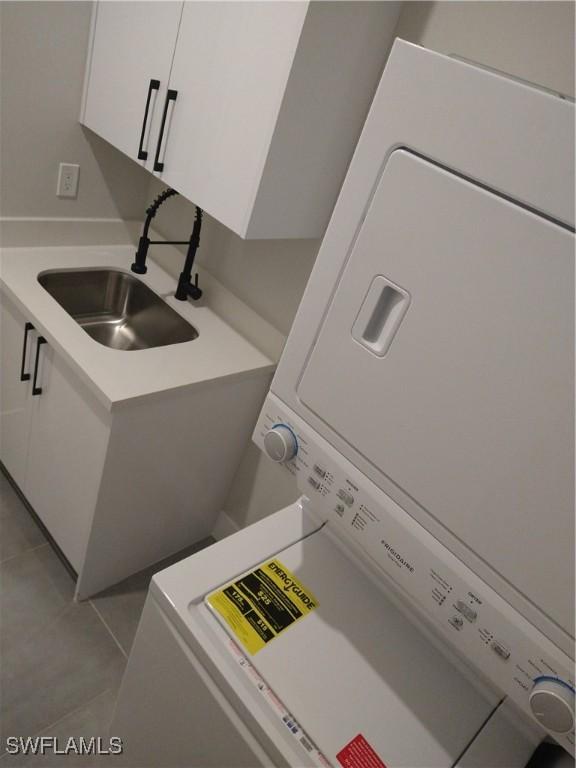 laundry room with sink, light tile patterned floors, cabinets, and stacked washer / drying machine