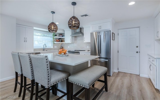 kitchen with wall chimney exhaust hood, stainless steel appliances, pendant lighting, light hardwood / wood-style floors, and white cabinets