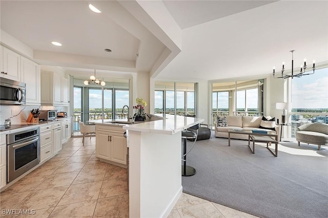 kitchen with light carpet, stainless steel appliances, pendant lighting, a center island with sink, and white cabinets