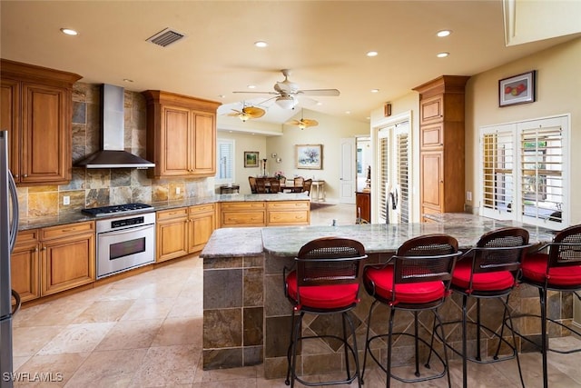 kitchen featuring stainless steel appliances, vaulted ceiling, a breakfast bar, and wall chimney range hood