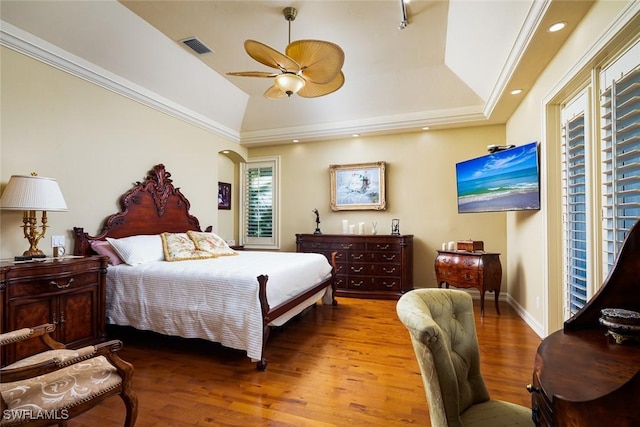 bedroom featuring vaulted ceiling, hardwood / wood-style floors, ornamental molding, ceiling fan, and a tray ceiling