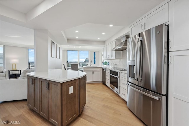 kitchen featuring white cabinetry, appliances with stainless steel finishes, light hardwood / wood-style floors, and wall chimney range hood