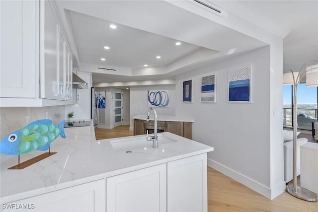 kitchen with light stone countertops, white cabinets, light wood-type flooring, and kitchen peninsula