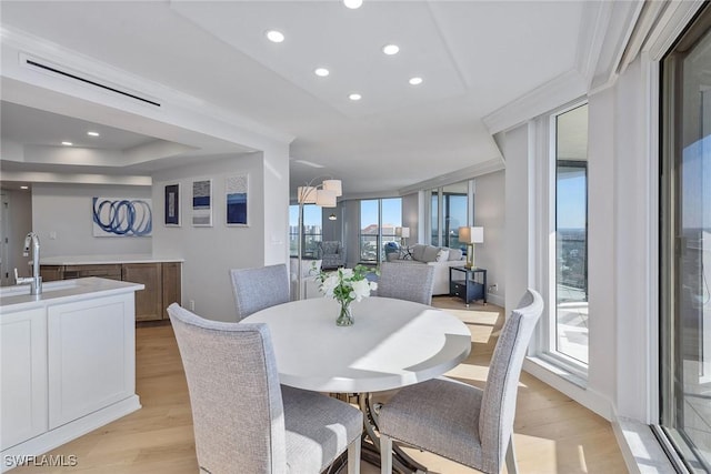 dining space featuring a raised ceiling, sink, and light hardwood / wood-style flooring