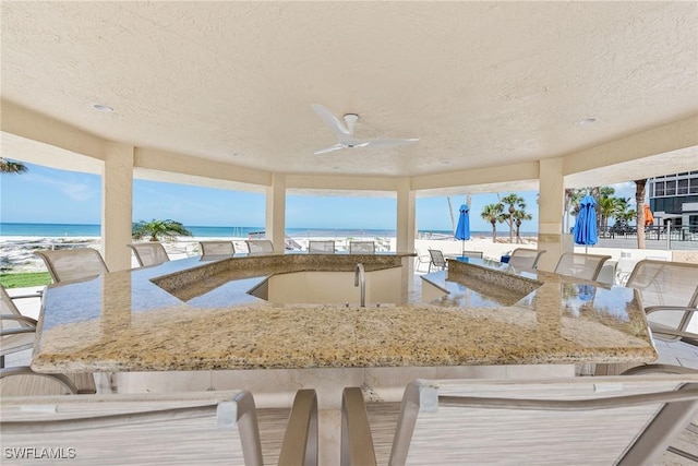 view of patio / terrace featuring a bar, a beach view, ceiling fan, and a water view