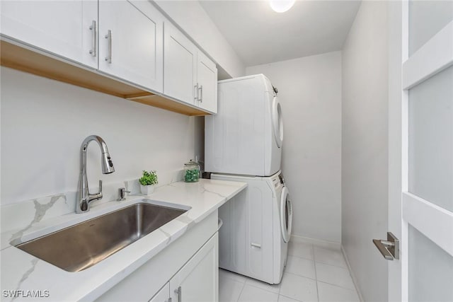 laundry area featuring stacked washer / dryer, sink, light tile patterned floors, and cabinets