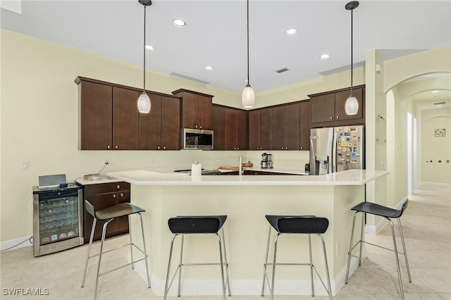 kitchen featuring decorative light fixtures, dark brown cabinetry, stainless steel appliances, and a center island with sink