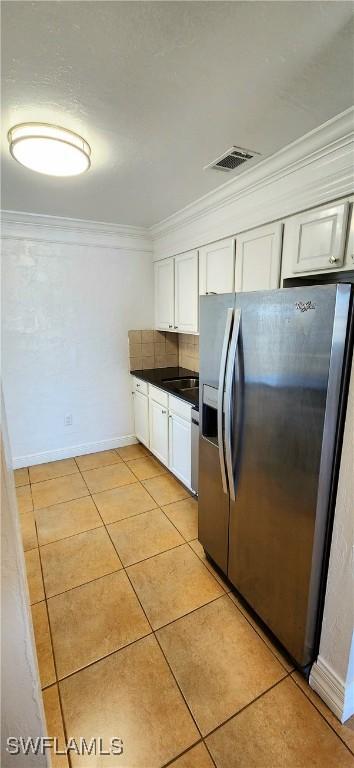 kitchen with stainless steel fridge with ice dispenser, light tile patterned floors, white cabinetry, and crown molding