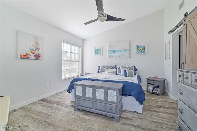 bedroom with a barn door, light hardwood / wood-style floors, vaulted ceiling, and ceiling fan