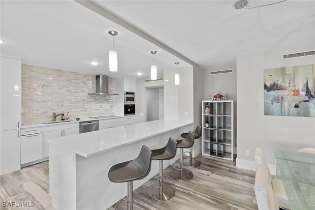 kitchen with kitchen peninsula, a breakfast bar, white cabinets, and wall chimney range hood