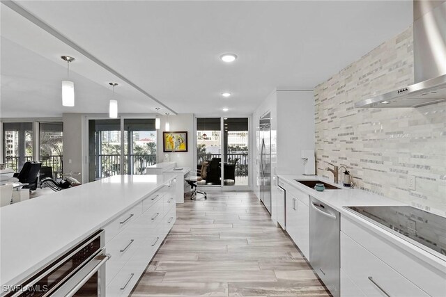 kitchen with appliances with stainless steel finishes, wall chimney range hood, sink, decorative light fixtures, and white cabinetry