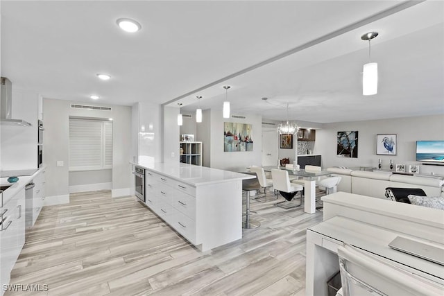 kitchen with appliances with stainless steel finishes, decorative light fixtures, white cabinetry, and light hardwood / wood-style floors